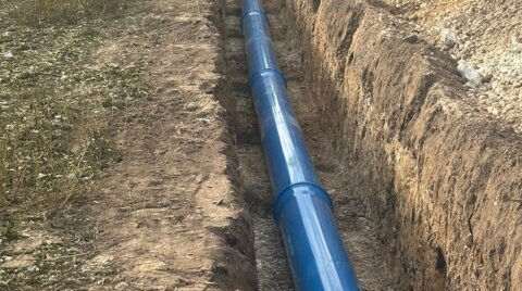 Long trench excavated across farmland with blue Molecor MoPVC pipe laid along the base