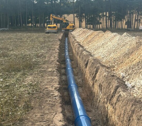 Long trench excavated across farmland with blue Molecor MoPVC pipe laid along the base