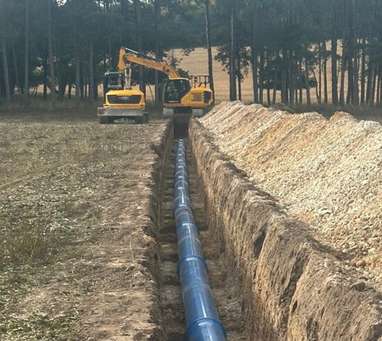 Long trench excavated across farmland with blue Molecor MoPVC pipe laid along the base