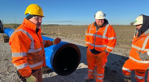 Three workers discussing installation details during an on-site training session, standing in front of a large-diameter pipe