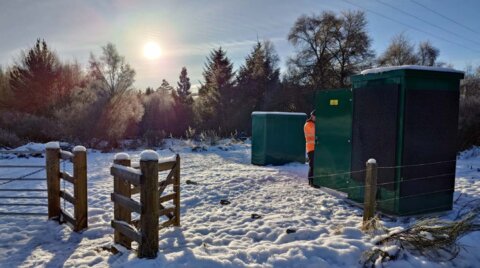 Two green water quality sampling kiosks in a snow-covered field, with an engineer standing beside one unit