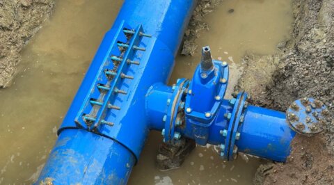 Under-pressure tee leaking on a live water network, visible within a flooded excavation trench prior to repair