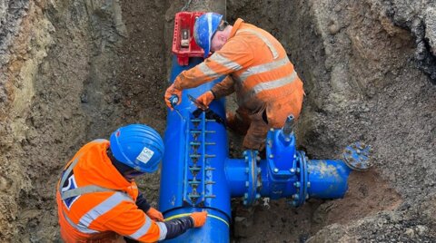 Two workers measuring a leaking under-pressure tee in a trench to accurately manufacture a bespoke encapsulation collar