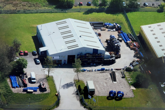 R2M Old Facility Aerial view of the original R2M facility showing a single warehouse building with limited external storage and pipework stock arranged around the yard