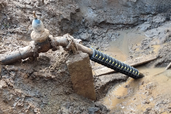 Connector clamp installed on an existing water main within a muddy excavation trench