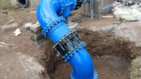 Completed emergency pipeline installation showing a large-diameter ductile iron fittings, bends and valve assembly supported on temporary blocks