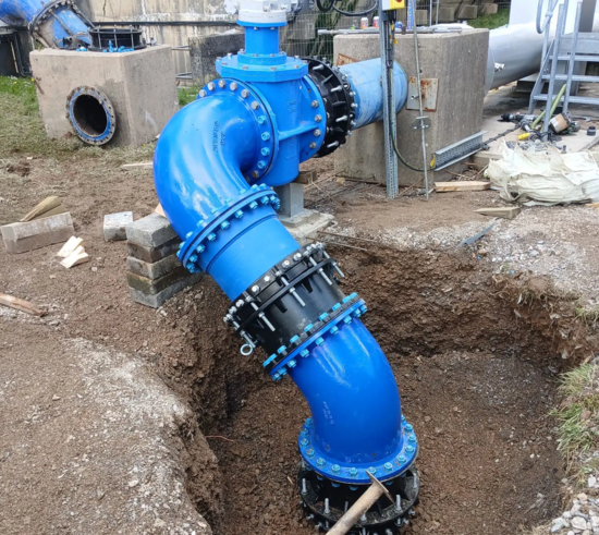 Completed emergency pipeline installation showing a large-diameter ductile iron fittings, bends and valve assembly supported on temporary blocks