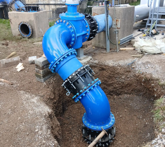 Completed emergency pipeline installation showing a large-diameter ductile iron fittings, bends and valve assembly supported on temporary blocks
