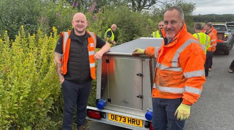 Two engineers wearing high-visibility clothing standing beside the rear of the trailer-mounted unit during on-site setup