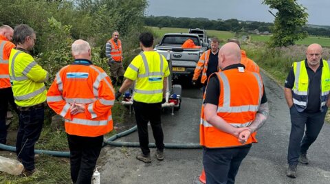 Group of engineers in high-visibility PPE gathered on a country road around the trailer unit during a site briefing