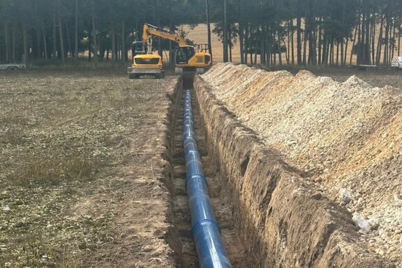 Long trench excavated across farmland with blue Molecor MoPVC pipe laid along the base