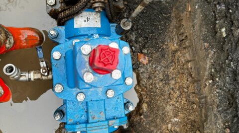 Top-down view of the EZ valve assembly during installation, showing an electric driver being used within a muddy excavation