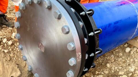 Close-up of a flange adaptor and blank flange at the end of a newly installed pipeline, with on-site workers inspecting the connection