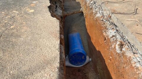Site operative installing Molecor MoPVC pipe in a narrow trench, with barriers and cones maintaining safe traffic flow