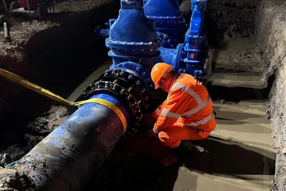 Engineer in high-visibility clothing inspecting a Multigrip fitting on a large-diameter pipeline within a deep excavation